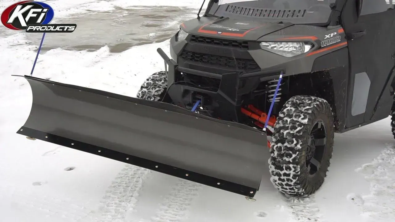 Black UTV with a snow plow blade clearing snow in a winter setting.