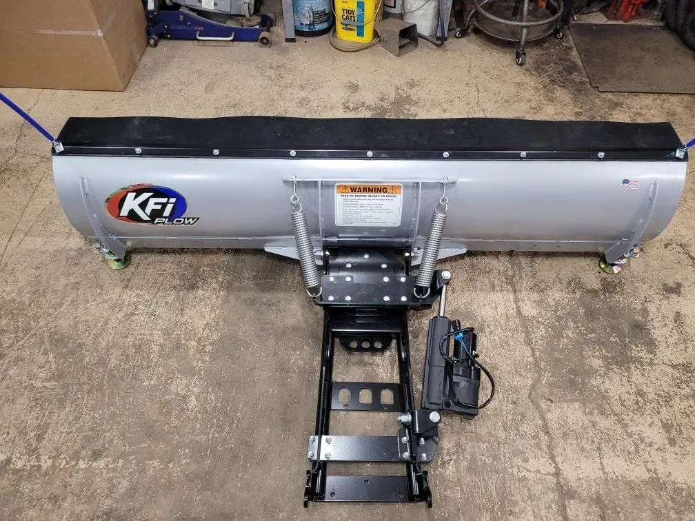 Silver KFI snow plow on a black frame, ready for installation, on a concrete floor.