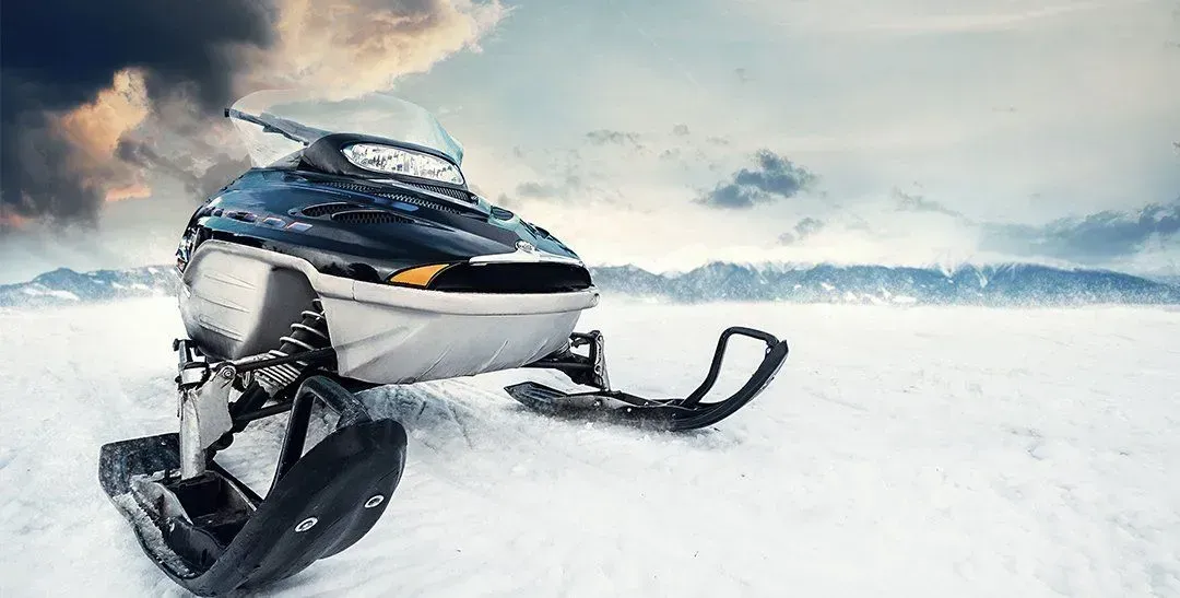 Snowmobile on a snowy plain against a cloudy mountain backdrop.