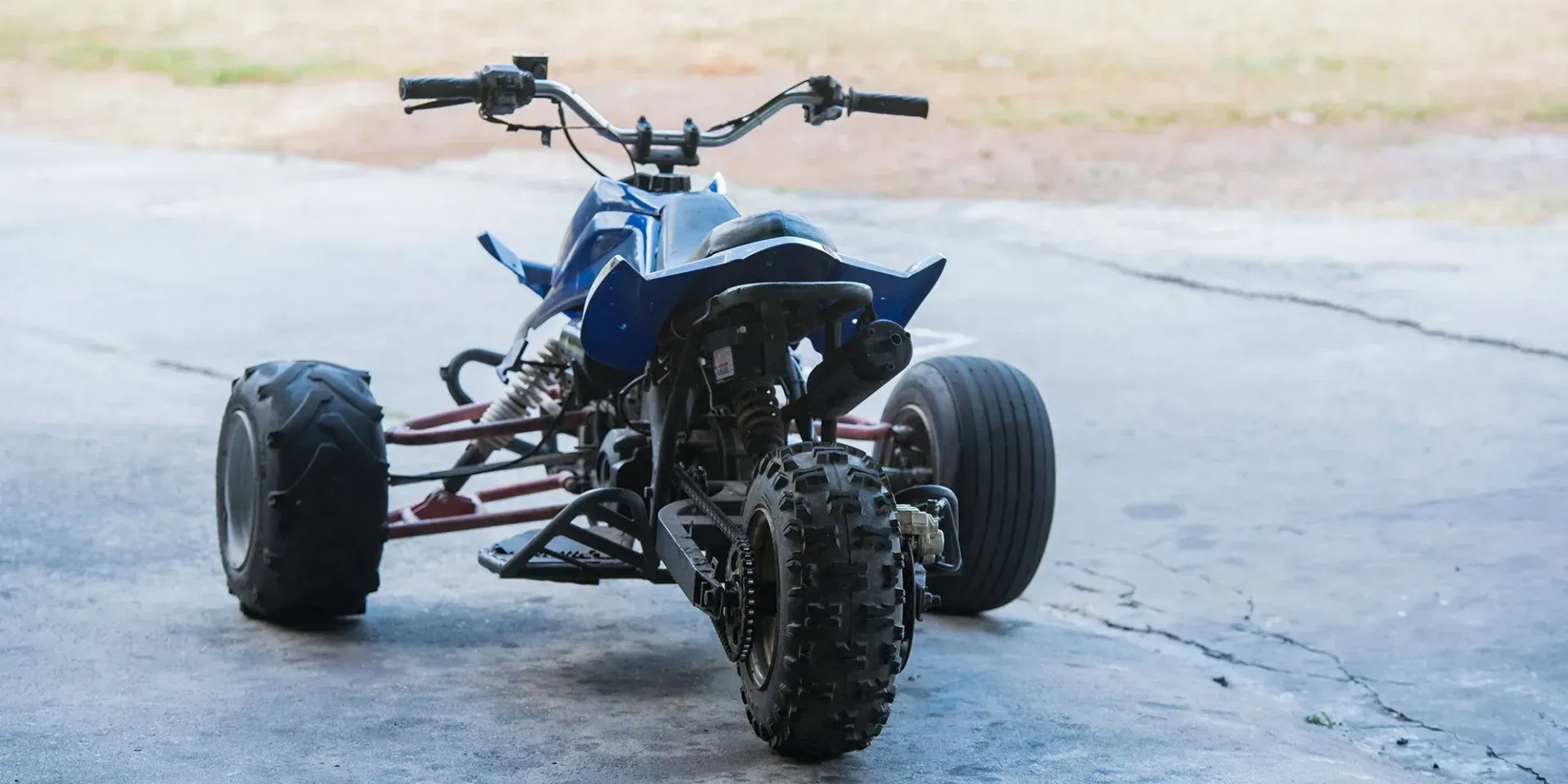 Blue sport ATV with knobby tires parked on a concrete pad