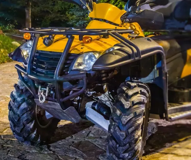 Front of a yellow utility ATV with knobby tires and a steel front rack