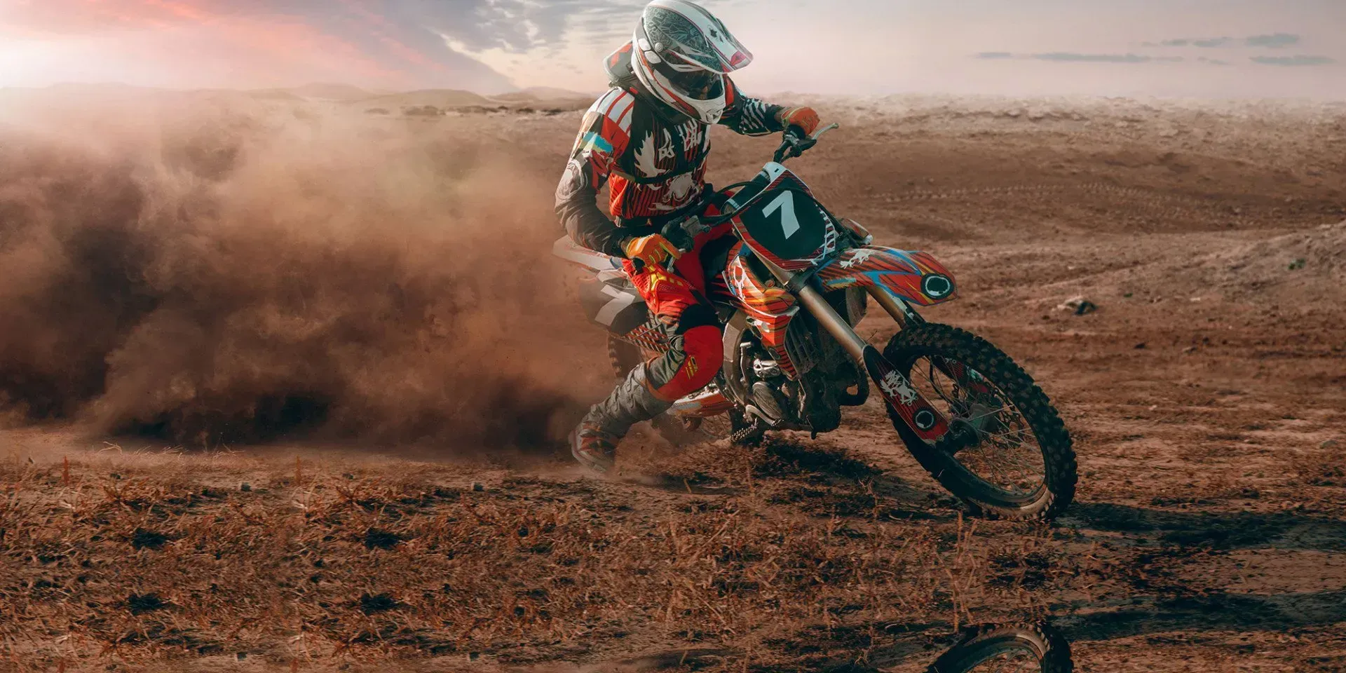 Motocross rider kicking up dust on an orange dirt bike