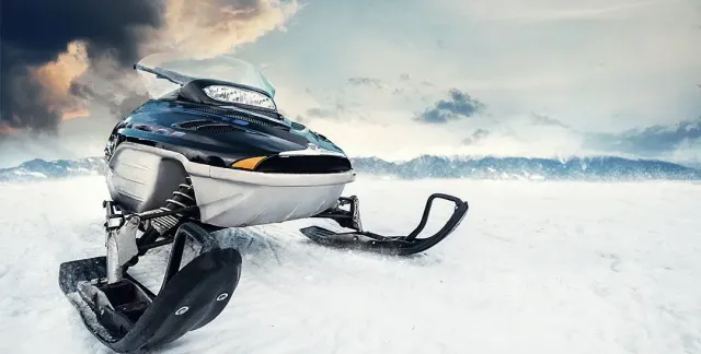Black and white snowmobile parked on open snow under a cloudy sky